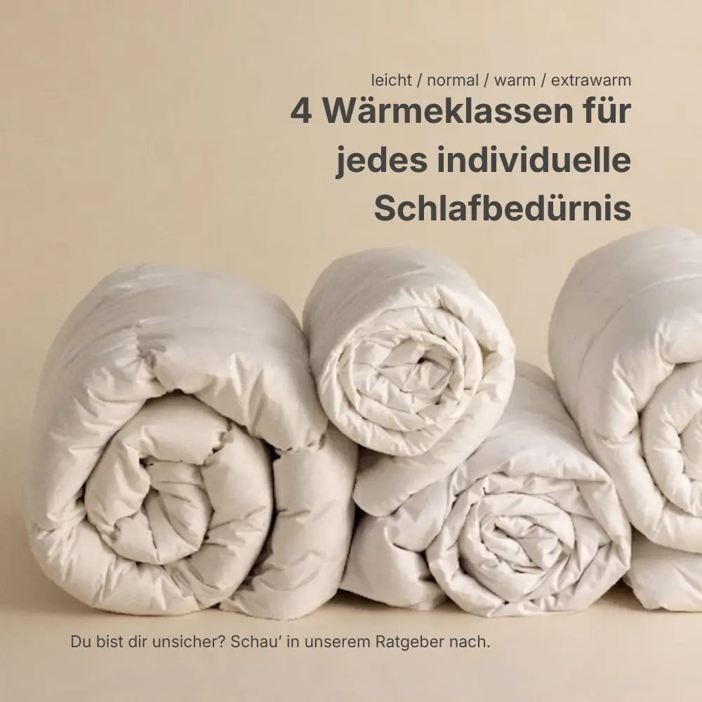 Mehrere gerollte Premium Daunen- und Federdecken nebeneinander, Darstellung von vier Wärmeklassen für individuelles Schlafbedürfnis von leicht bis extrawarm