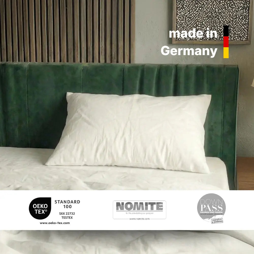 Weißes Essential Federkissen auf einem Bett mit Hinweis ‚made in Germany‘ und eingeblendeten Zertifikatslogos.