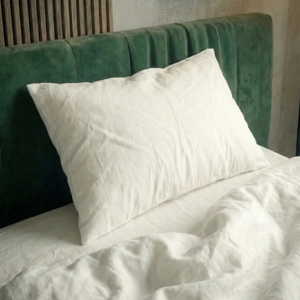 Weißes Essential Federkissen liegt auf einem Bett vor einem grünen, gepolsterten Kopfteil.