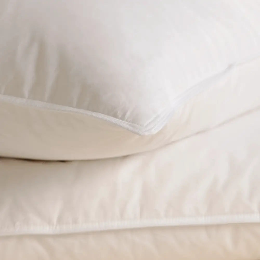 Detailansicht von zwei weißen Essential Federkissen, übereinanderliegend auf einer hellen Oberfläche.