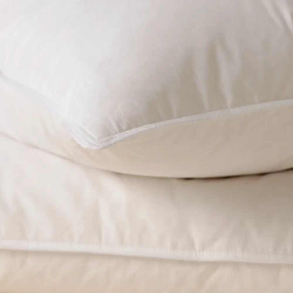 Detailansicht von zwei weißen Premium Daunenkissen, übereinanderliegend mit sichtbaren Kissenkanten.