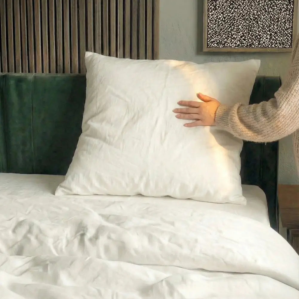 Weißes Essential Federkissen auf einem Bett, eine Hand drückt leicht auf die Kissenoberfläche.