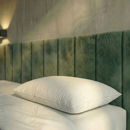 Weißes Premium Daunenkissen liegt flach auf einem Bett vor einem grünen, gepolsterten Kopfteil.