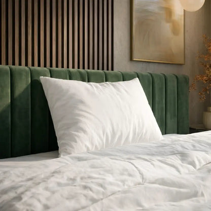 Weißes Essential Federkissen mit glattem Bezug auf einem Bett mit grünem, gepolstertem Kopfteil.