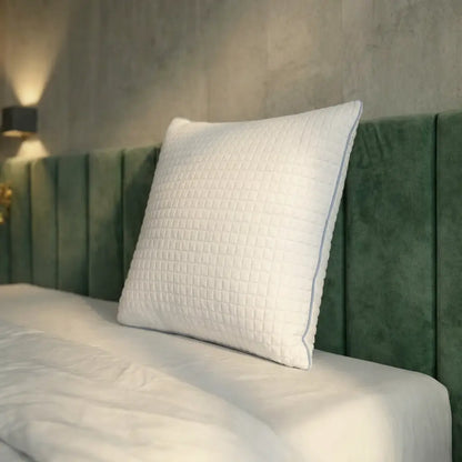 Weißes Essential Kühlkissen mit strukturierter Oberfläche auf einem Bett mit weißer Bettwäsche und grünem Kopfteil